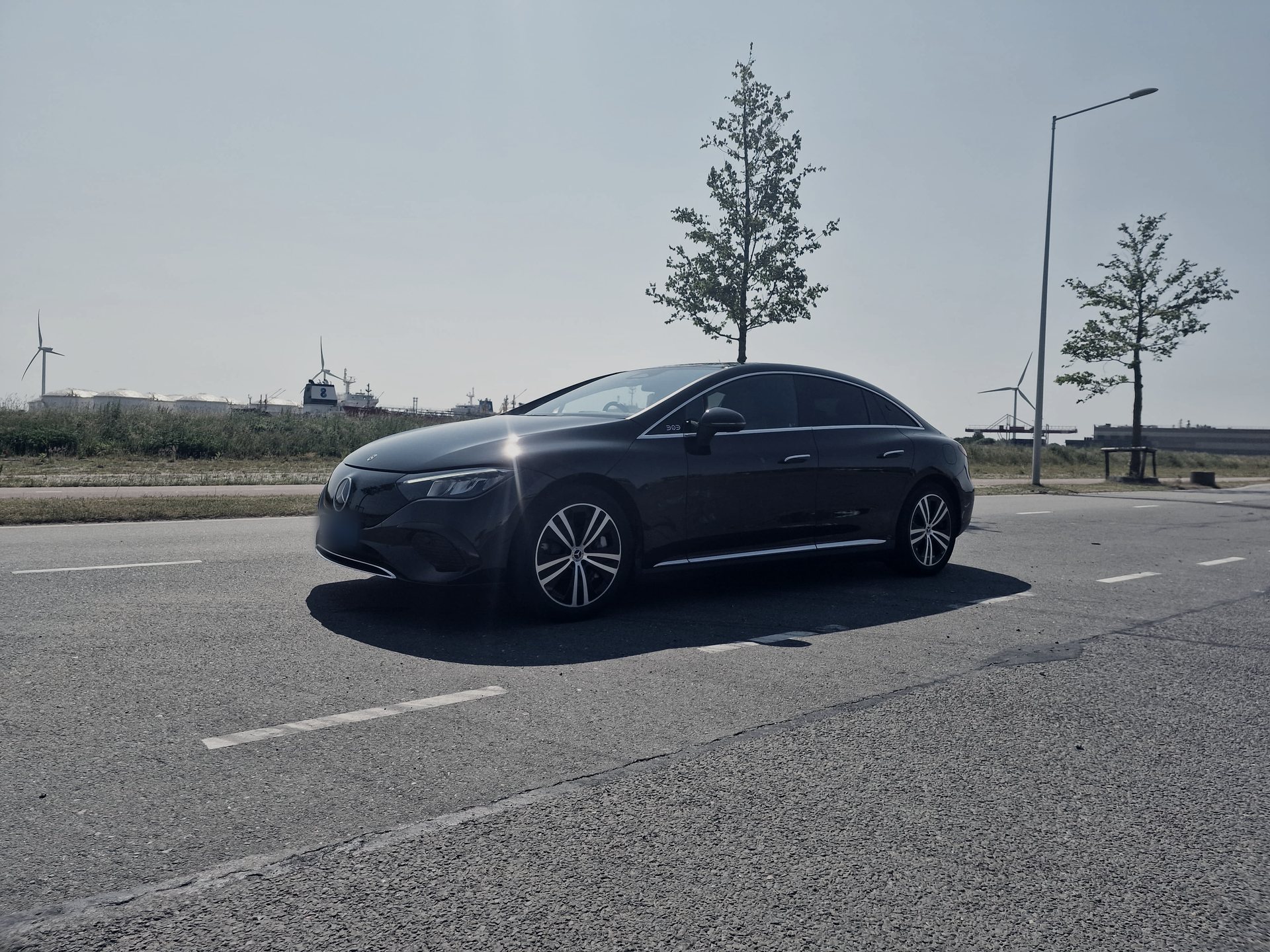 Black Mercedes-Benz EQE of AmstelCab Business Class on an open road by the water, wind turbines behind