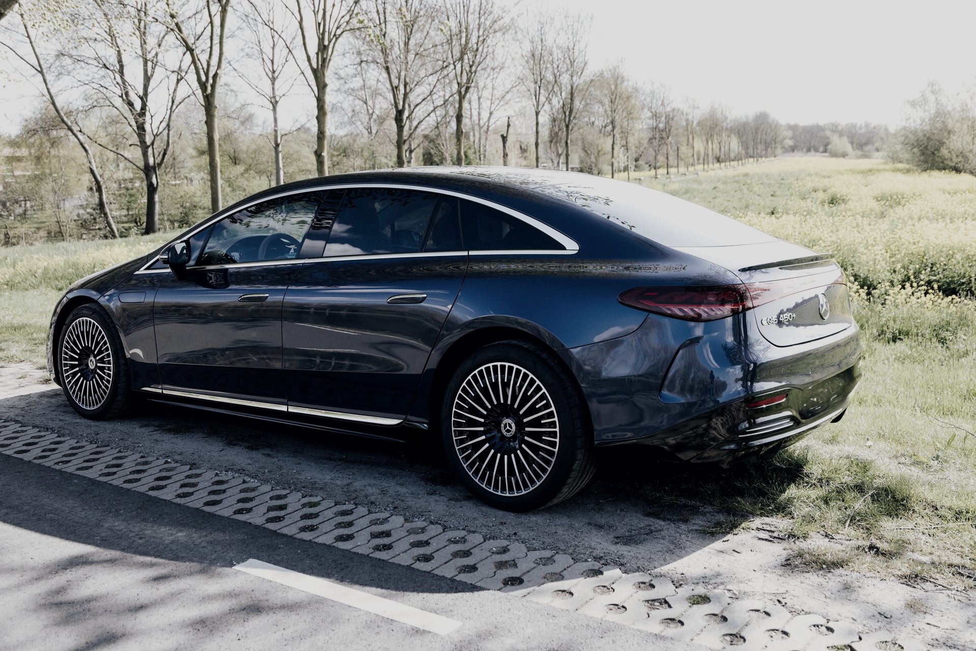 Mercedes-Benz EQS, electric First Class, on a country road beside a flowering field