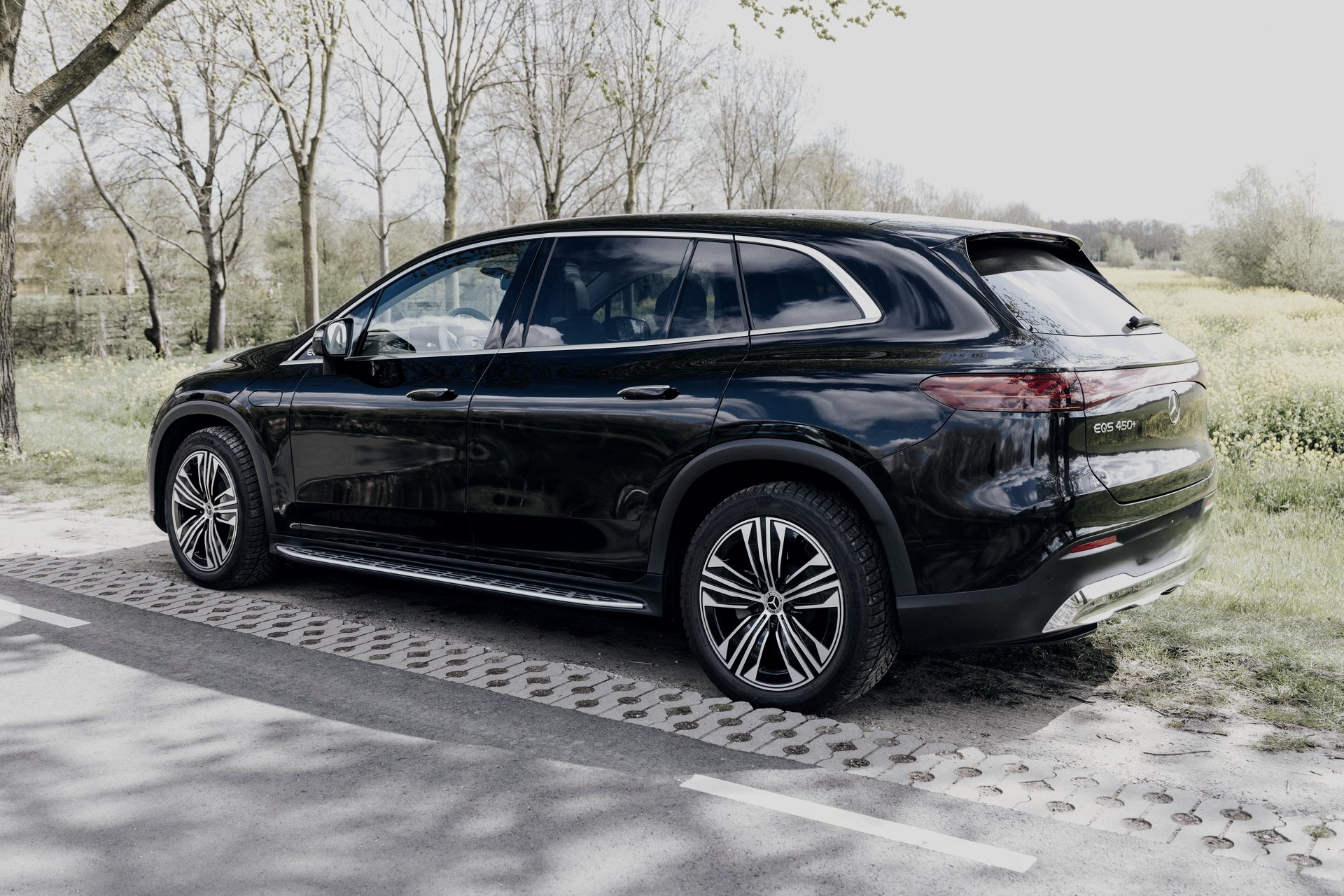 Black Mercedes-Benz EQS SUV, electric First Class, on a tree-lined road outside the city