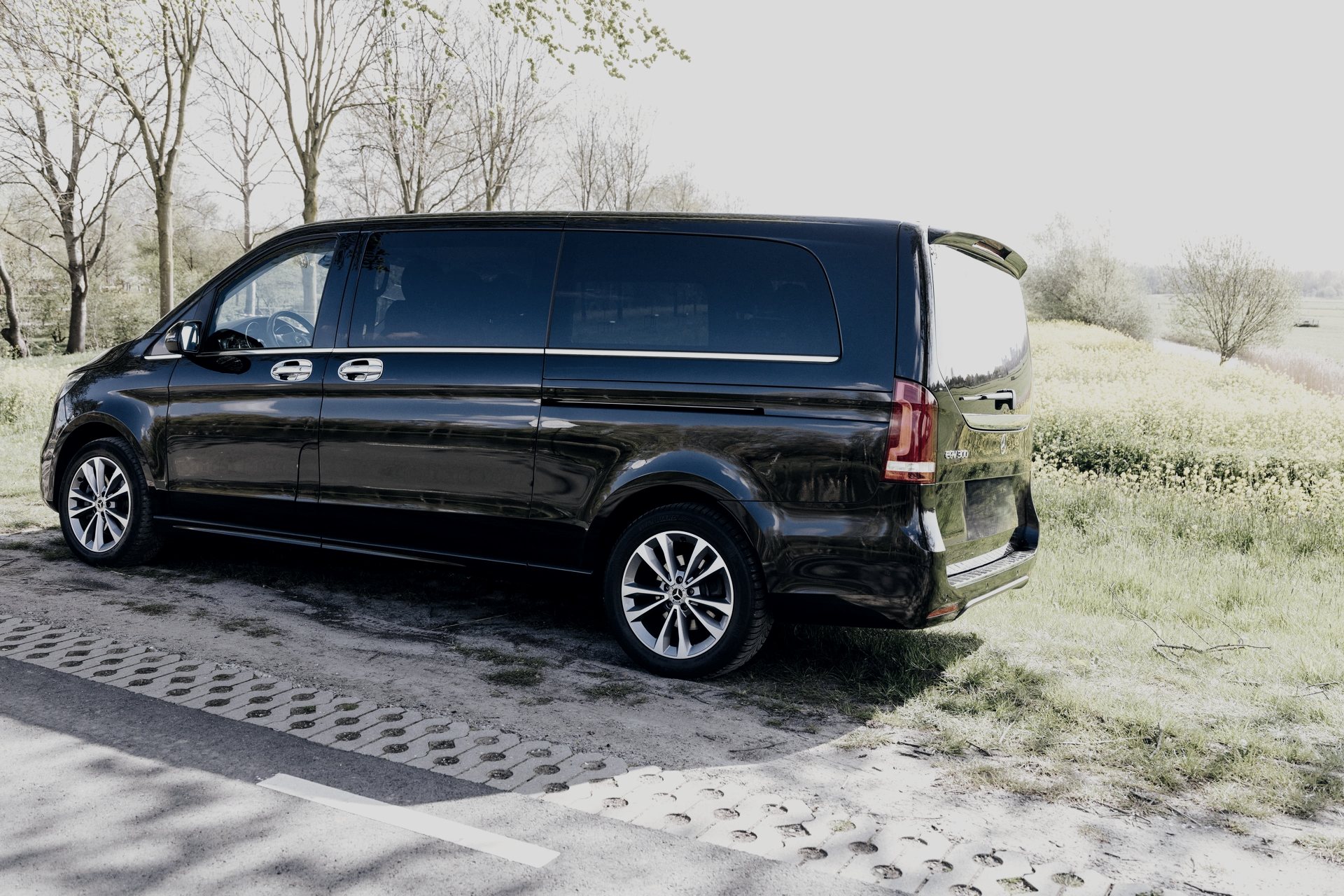 Black Mercedes-Benz EQV of the AmstelCab Van Class on a country road beside a flowering field