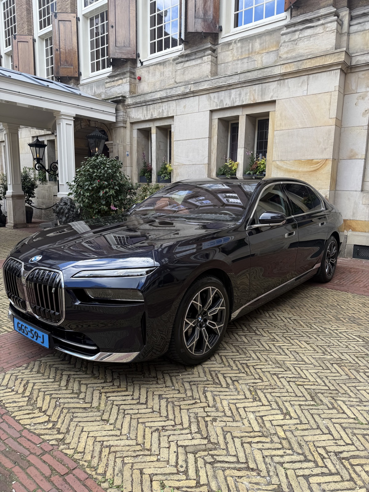 The black BMW i7 on the herringbone brick courtyard of the Sofitel Legend The Grand in Amsterdam, seen from the front three-quarter