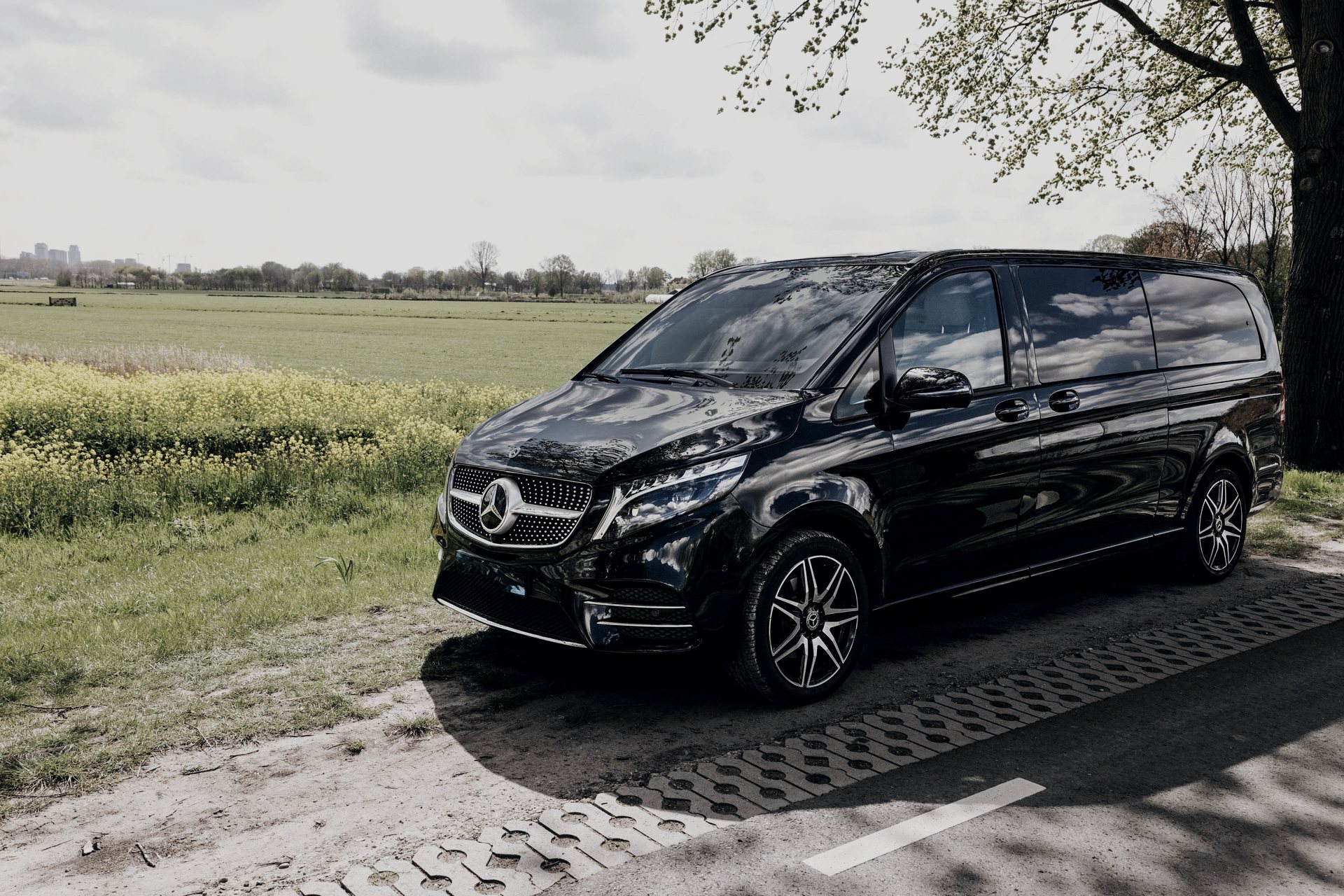 Black Mercedes-Benz V-Class of the AmstelCab Van Class on a country road, the Amsterdam skyline on the horizon